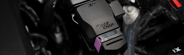 RaceChip S Steuergerät Nahaufnahme im Motorraum, schwarzes Gehäuse mit RaceChip-Logo, Produktbezeichnung und violettem Serienstecker.
